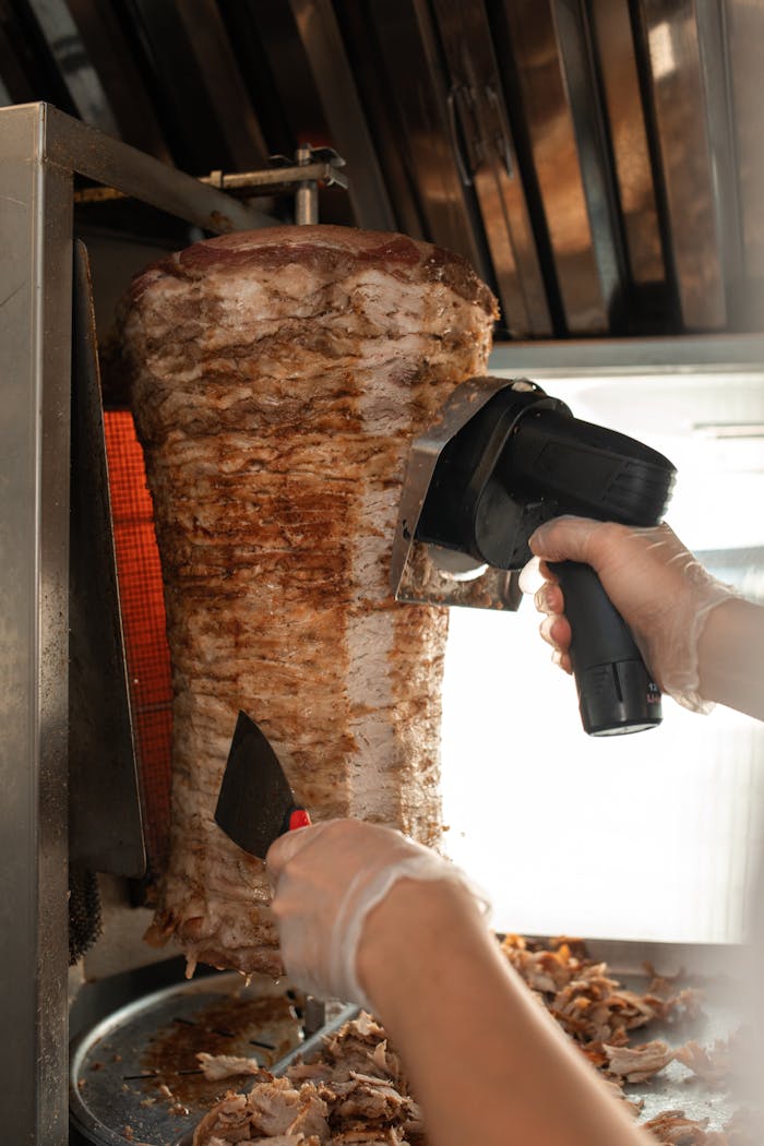 about-03 Close-up view of shawarma being sliced with professional equipment in a kitchen.