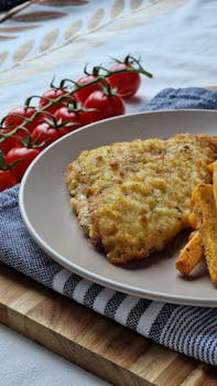 pexels photo 32651694 32651694 Tasty breaded schnitzel with crispy fries and fresh cherry tomatoes on a wooden table.